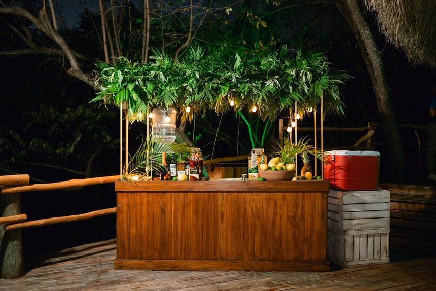 Outdoor bar with leafy roof & drinks by a wooden railing at Morgan's Rock, a sustainable jungle lodge near San Juan del Sur