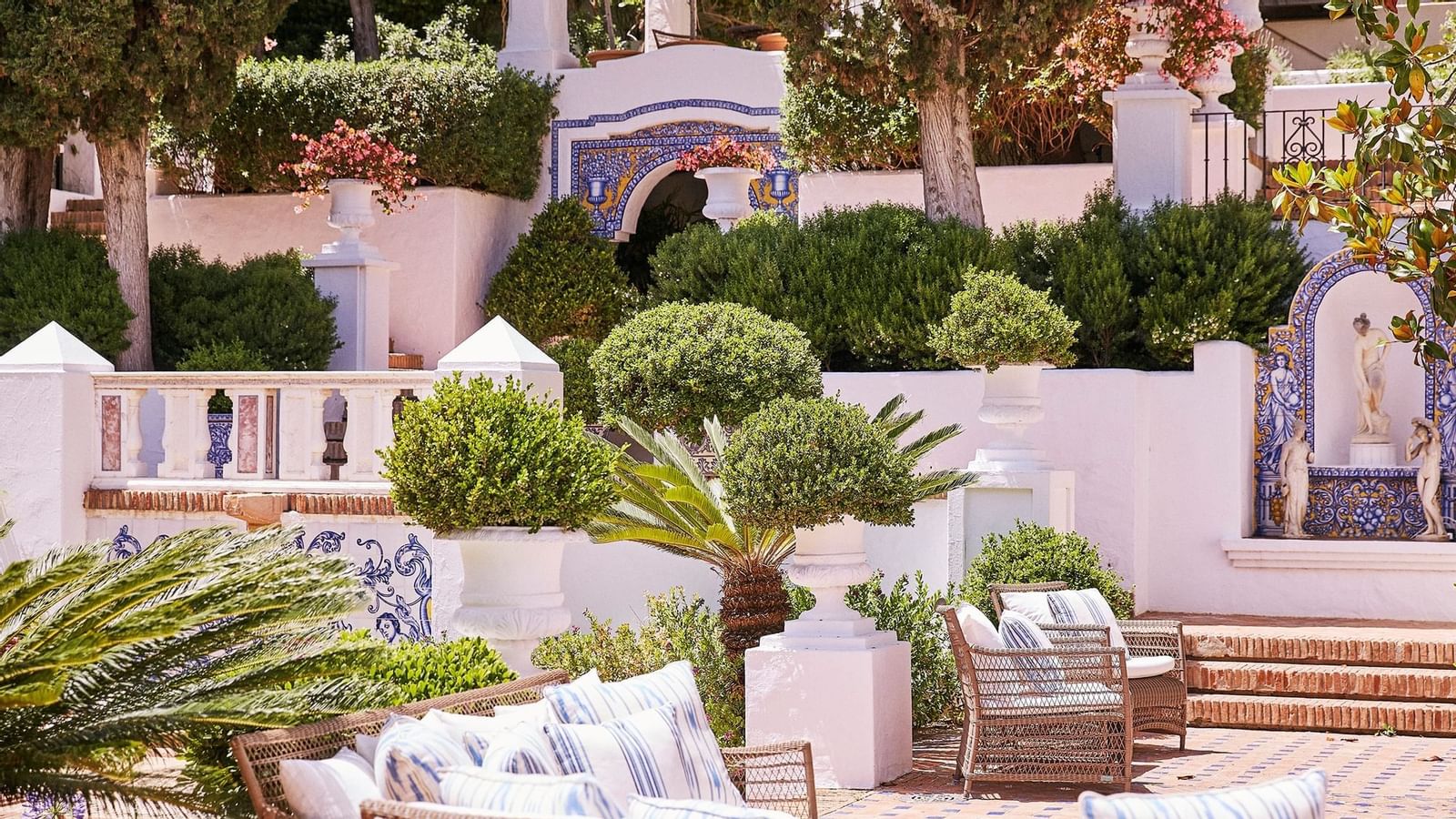 Outdoor wicker sofa and cushions placed near a swimming pool, with tall palm trees in the background at Marbella Club