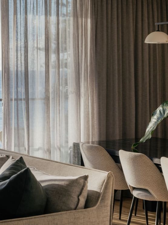Coastal Three Bedroom Suite at Elysium Hotels dining table and sofa by sheer curtains overlooking the blue ocean