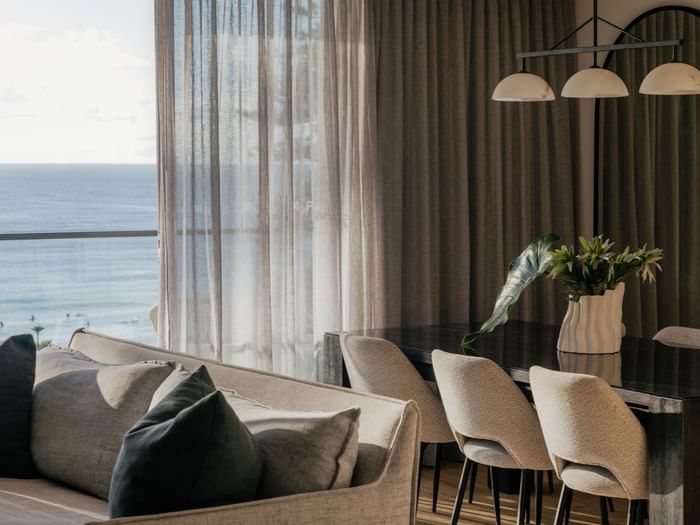 Coastal Three Bedroom Suite at Elysium Hotels dining table and sofa by sheer curtains overlooking the blue ocean