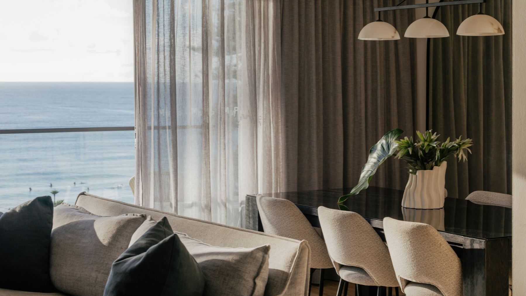 Coastal Three Bedroom Suite at Elysium Hotels dining table and sofa by sheer curtains overlooking the blue ocean
