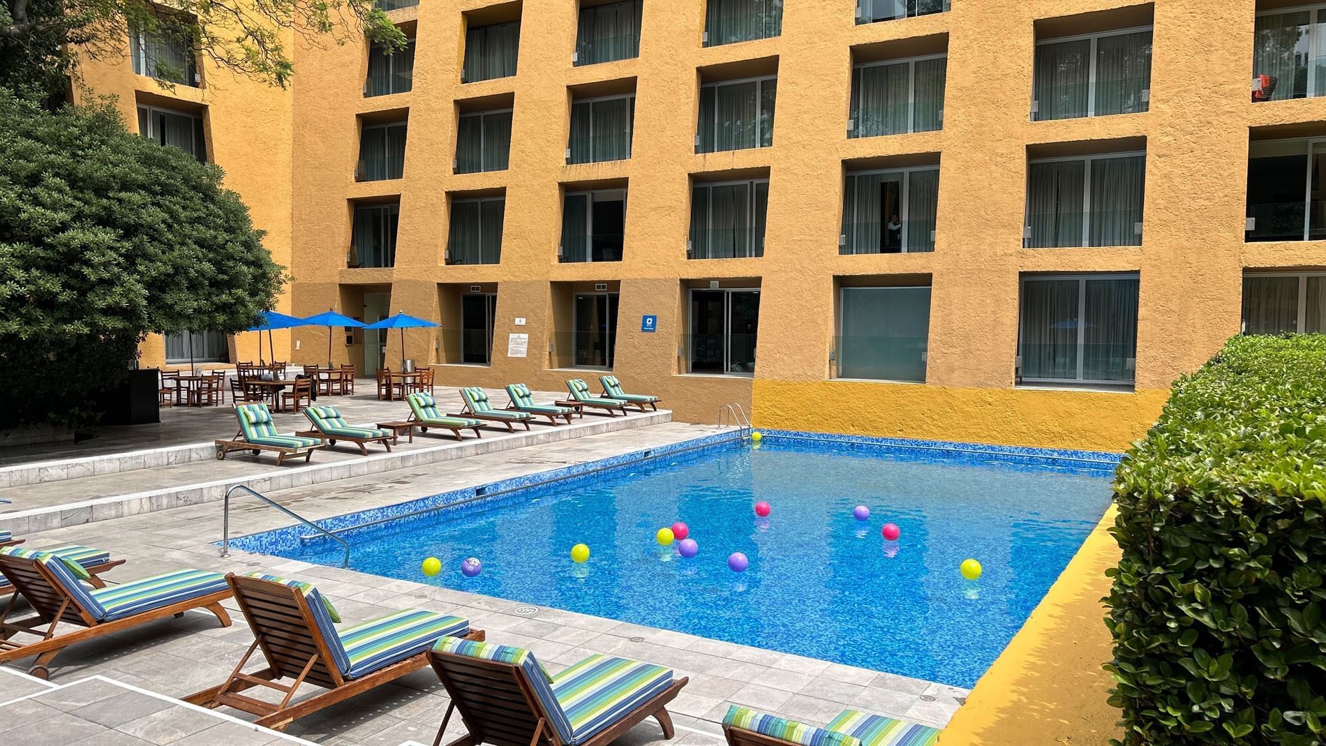 Outdoor swimming pool with striped loungers and yellow hotel exterior at Camino Real Polanco Mexico
