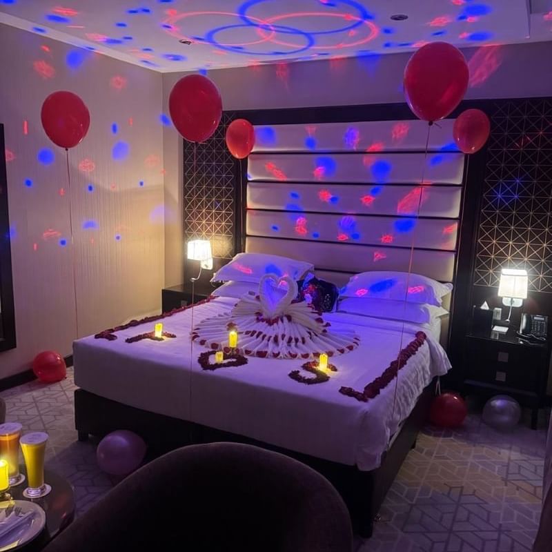 Room at Warwick Hotels and Resorts decorated for a special occasion, with rose petals, candles, and a towel swan on the bed