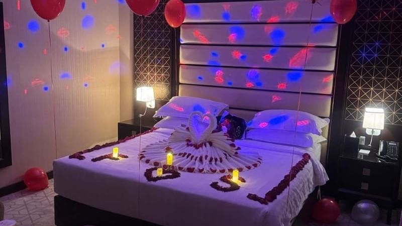Room at Warwick Hotels and Resorts decorated for a special occasion, with rose petals, candles, and a towel swan on the bed