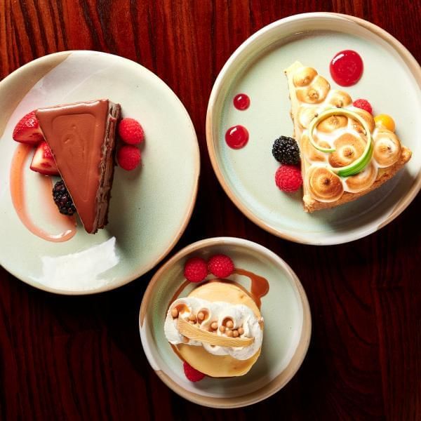 An overhead shot of three plates of desserts, including chocolate cake, key lime pie with a toasted meringue topping, and a caramel dessert topped with whipped cream.