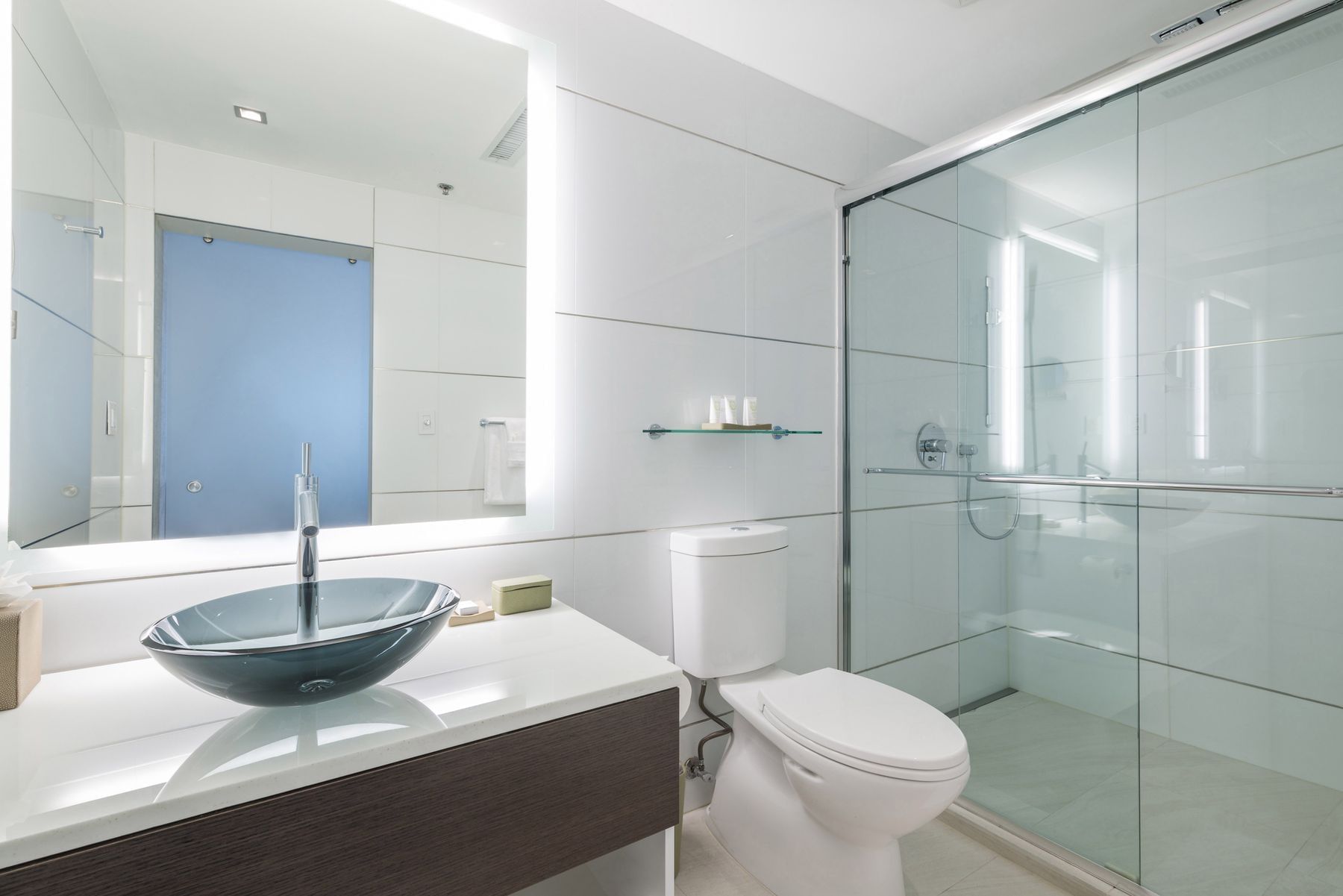 A modern bathroom with a glass-enclosed shower, white toilet, and blue glass basin