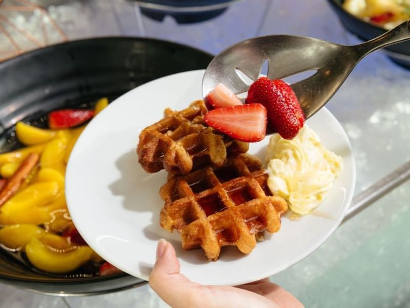 Hand holding a plate with a waffle, strawberries served in a restaurant at Crown Hotels Perth