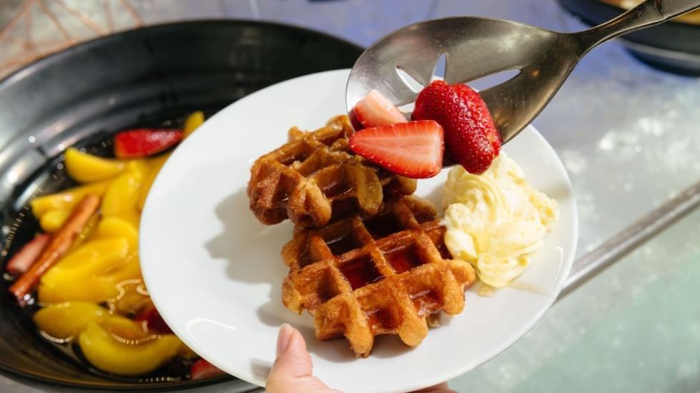 Hand holding a plate with a waffle, strawberries served in a restaurant at Crown Hotels Perth