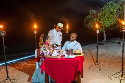 A couple sitting at a beachside table and a person served champaign in La Mar at Hotel Isla Del Encanto