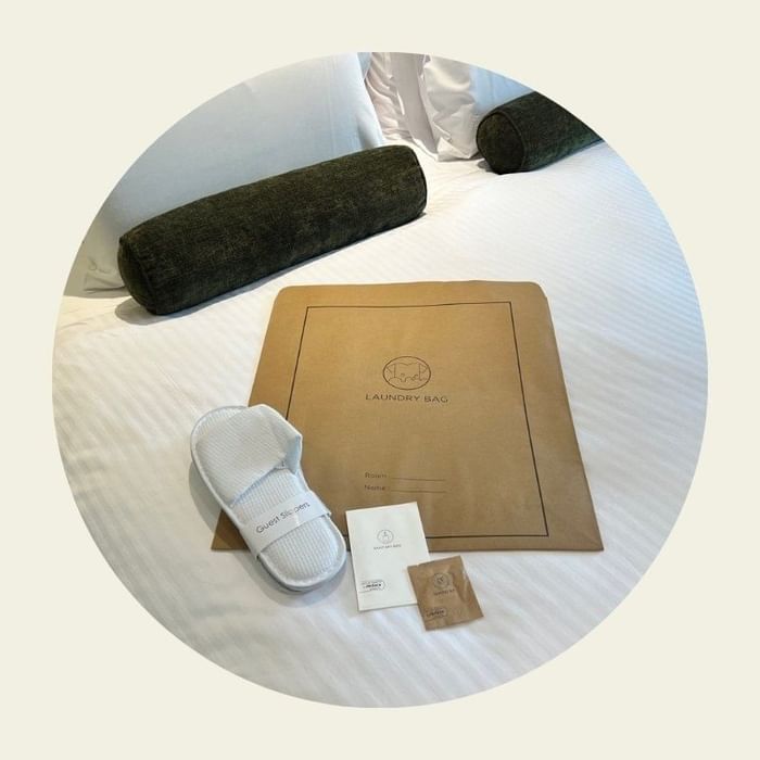 Laundry bag, white slippers, and care cards arranged on a neatly made bed at Novotel Darling Square