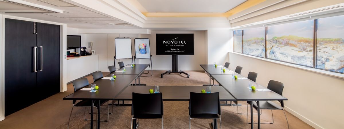 U-shape table set up facing TV by the windows in the Waratah Conference Room at Novotel Sydney International Airport 