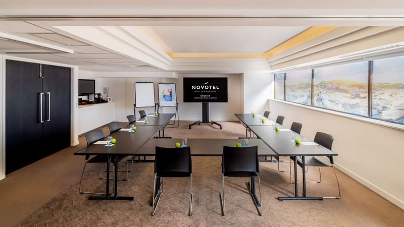 U-shape table set up facing TV by the windows in the Waratah Conference Room at Novotel Sydney International Airport 