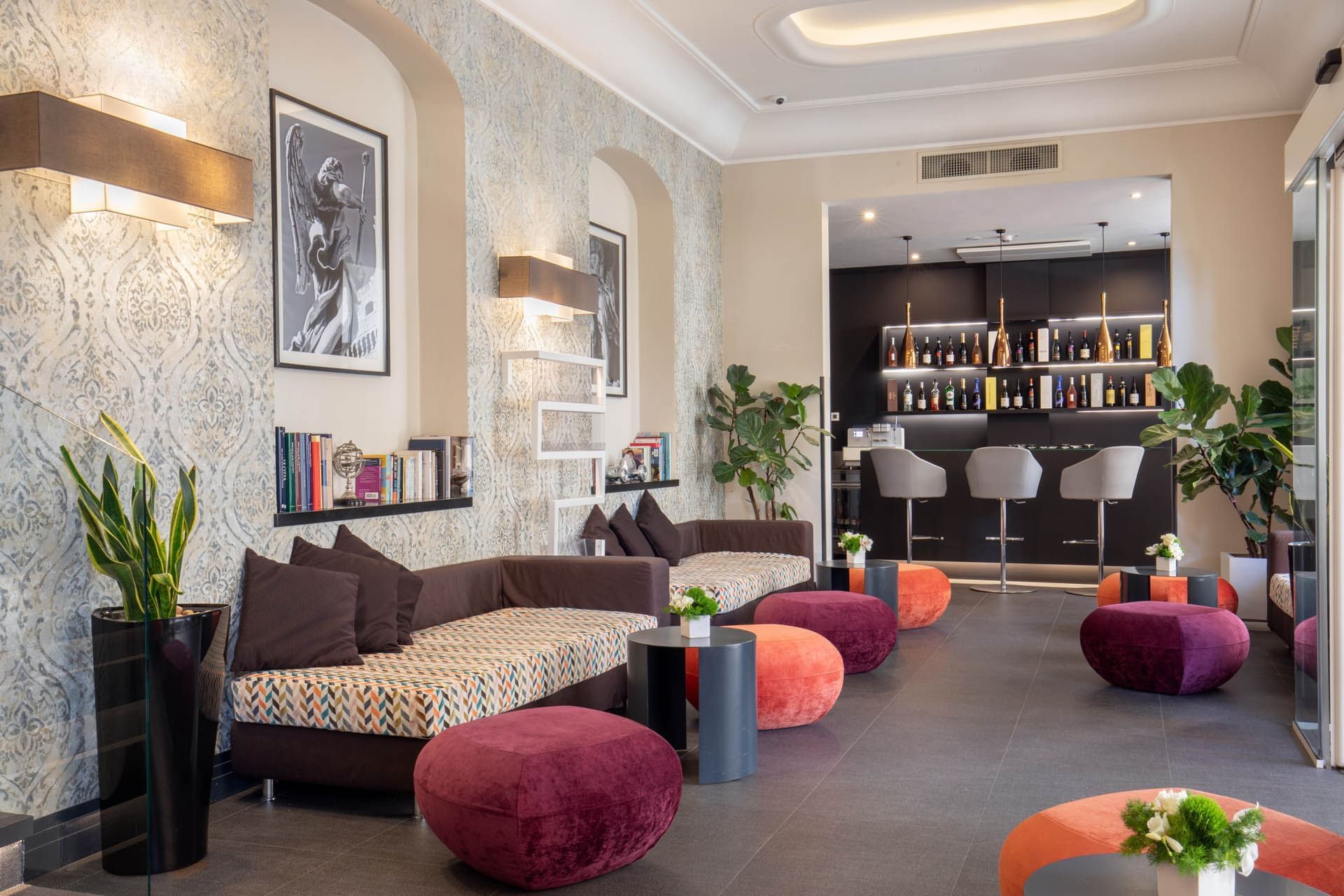 Lounge area with patterned sofas, poufs, bookshelves, and a bar featuring a variety of drinks at The Republic Hotel