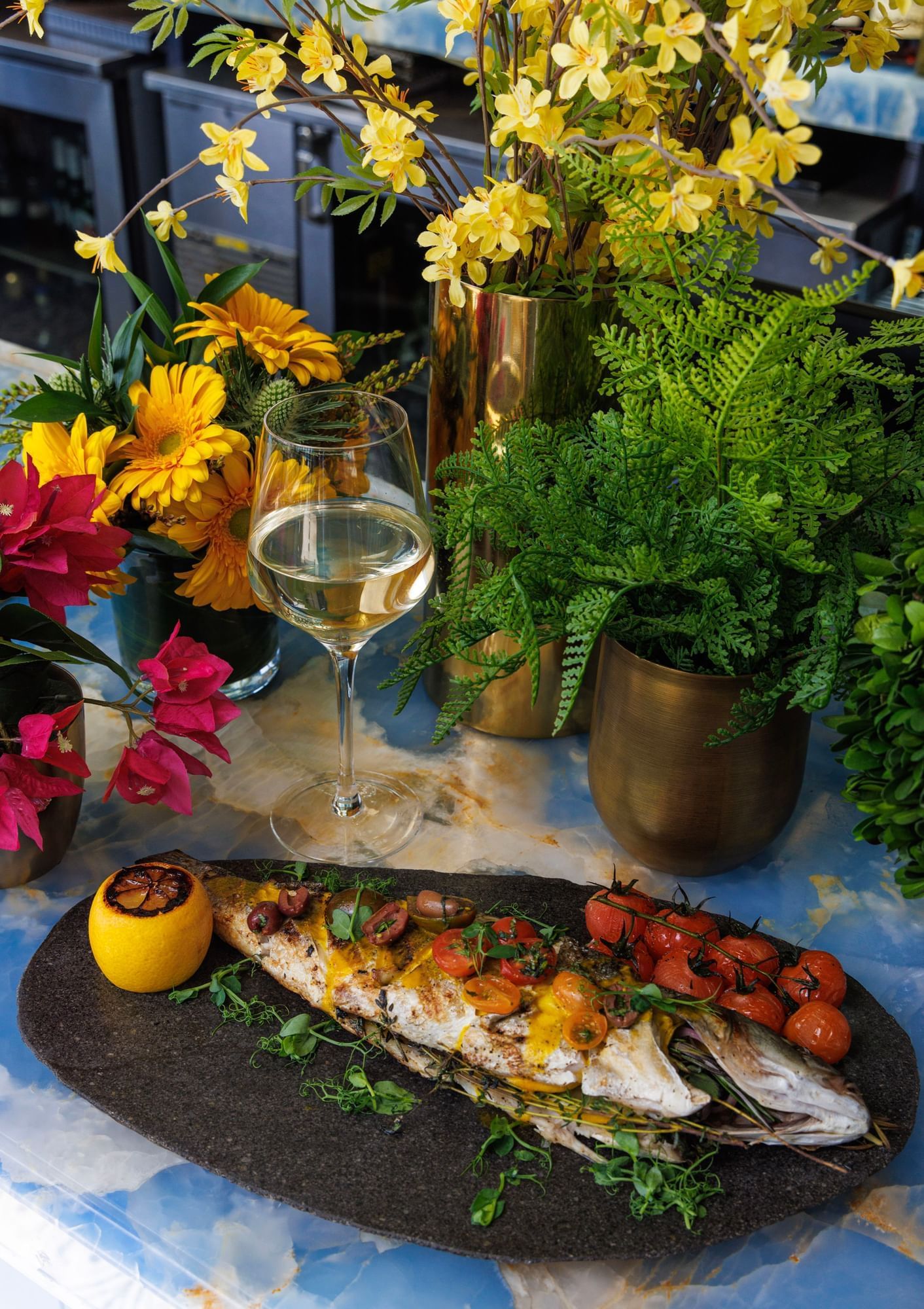 A plate of fish and flowers on a table with a glass of wine	