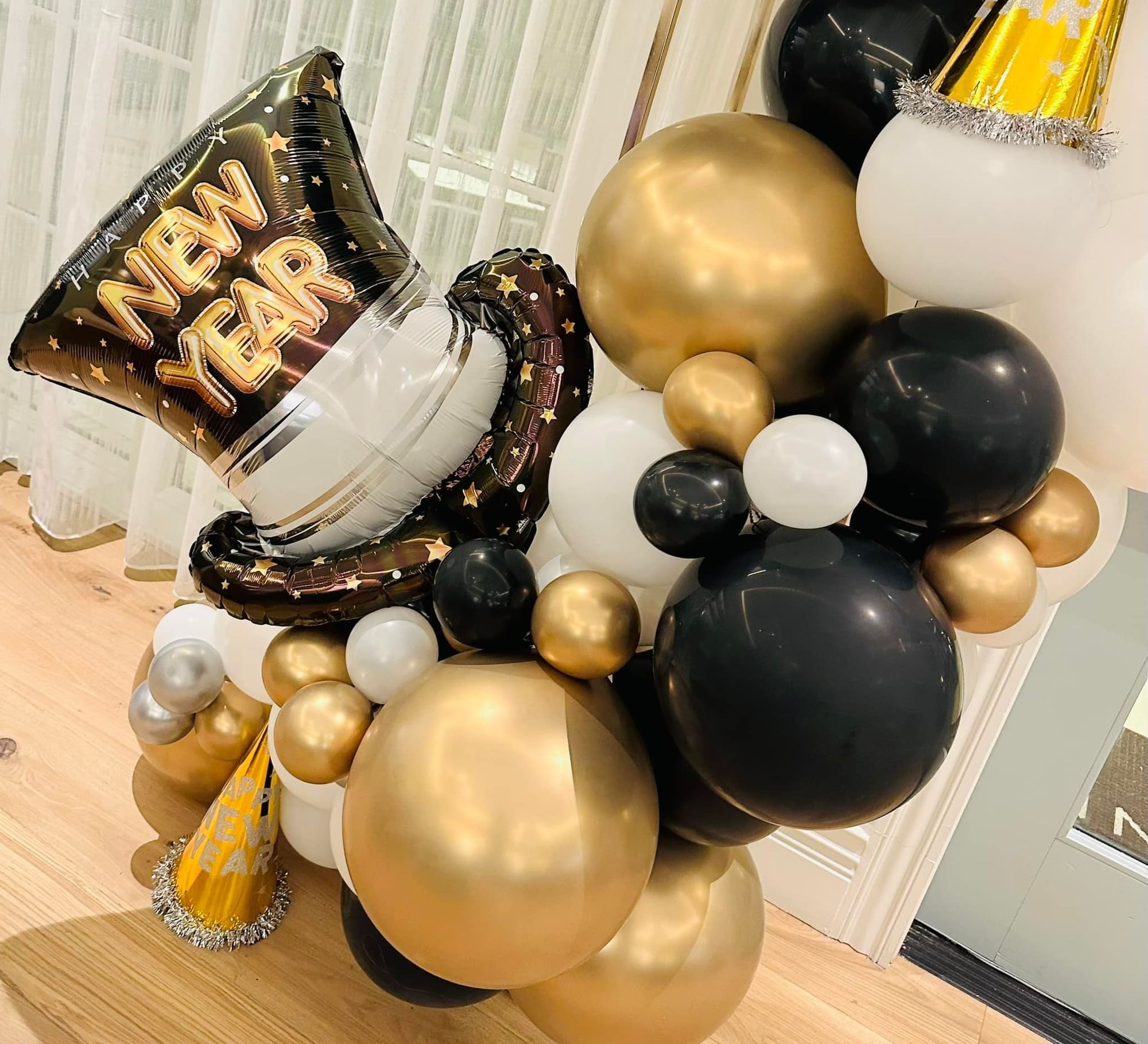 A New Year balloon arrangement with black, gold, and white balloons and two party hats.