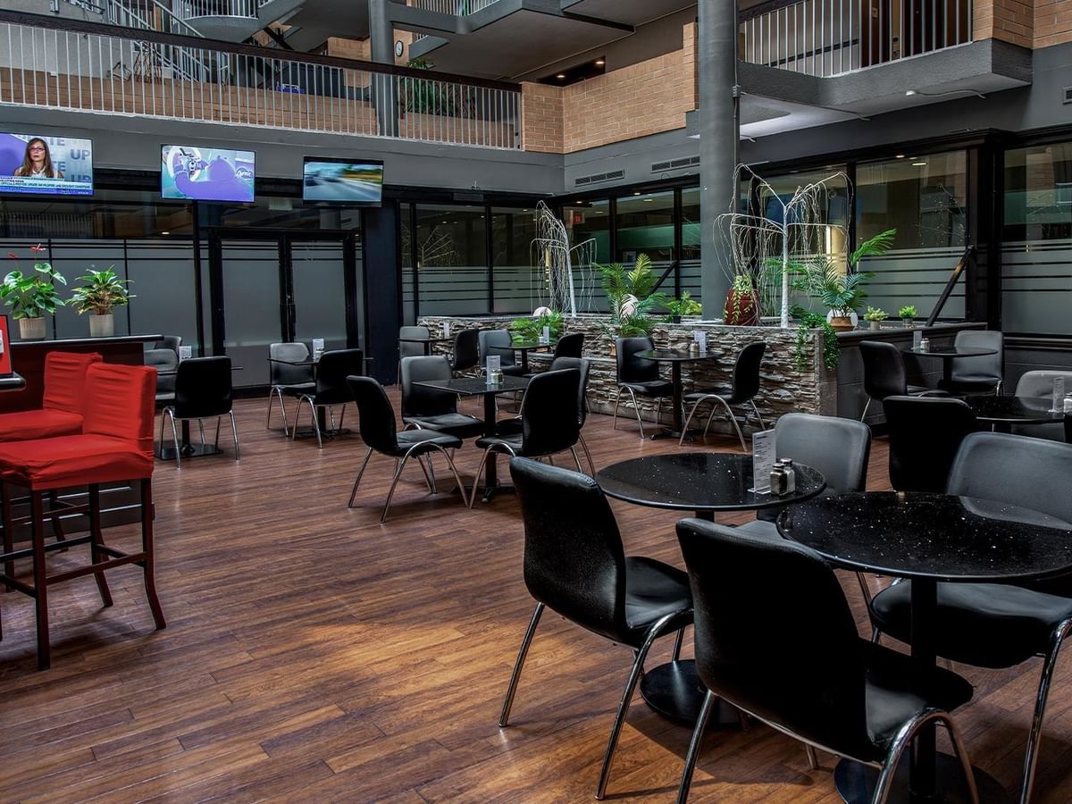 Modern dining area with dark tables, red bar seating, and greenery at Rockies Bar & Grill, Coast Calgary University Area Hotel by APA.