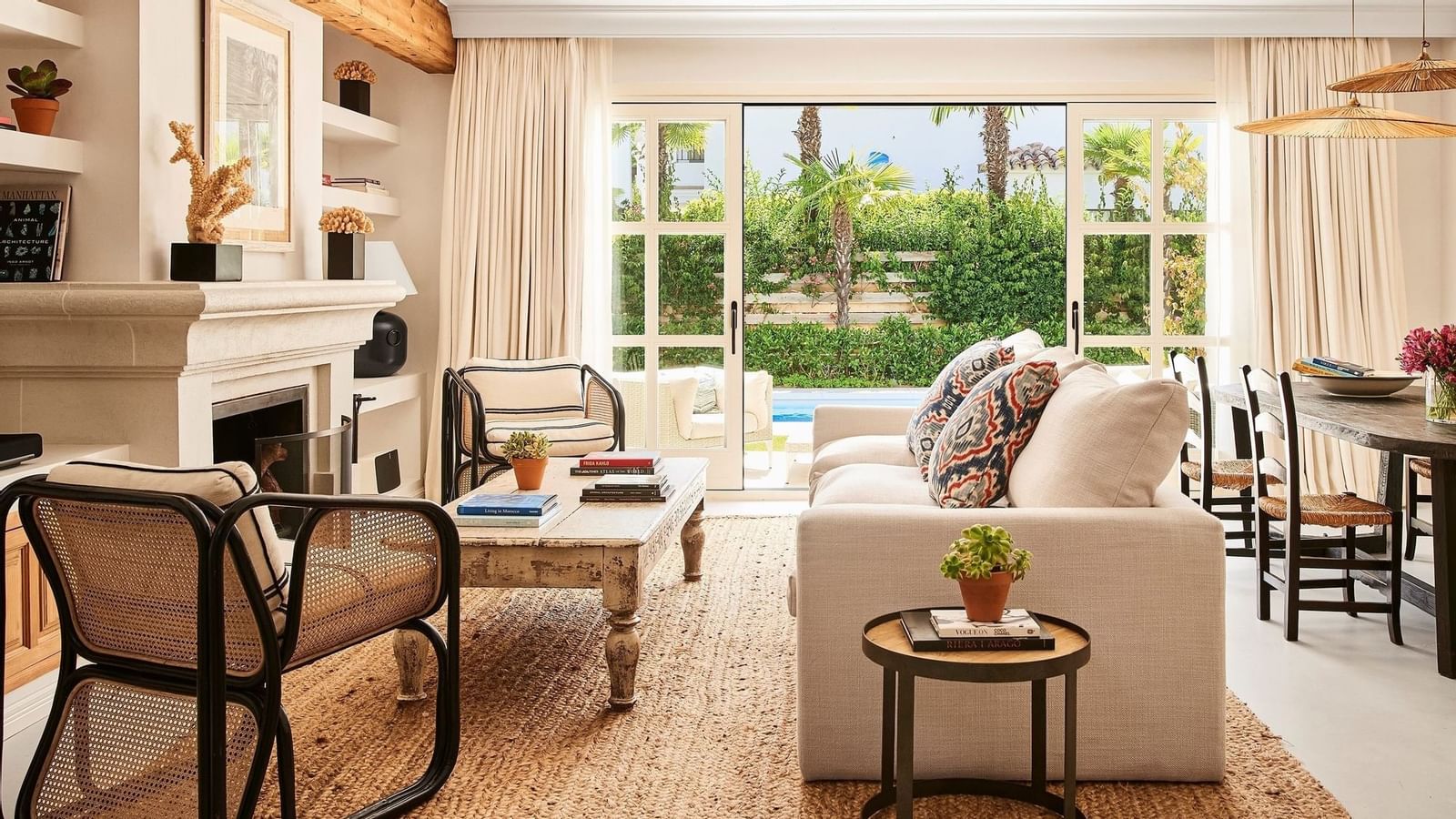 Living room with white sofa and rattan chairs placed near a stone fireplace and patio doors at the Marbella Club