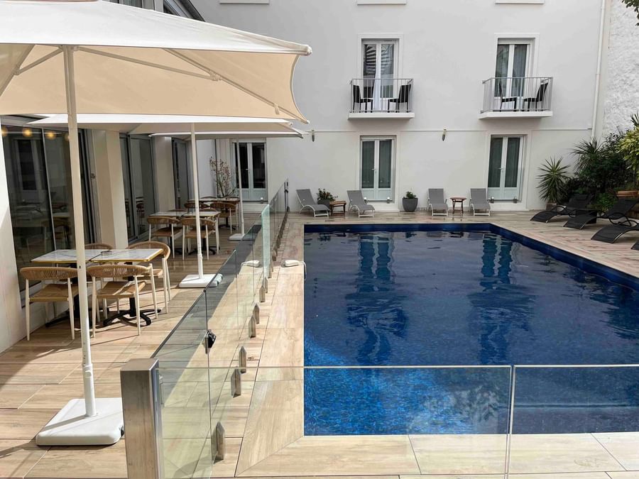 Piscine bleue avec terrasse et tables en plein air à l'Hôtel Le Yachtman.
