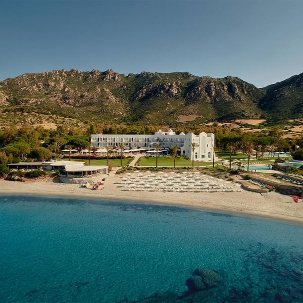 Ein luxuriöses Hotel am Strand mit weißen Liegen und Meerblick, umgeben von Bergen und grüner Vegetation.