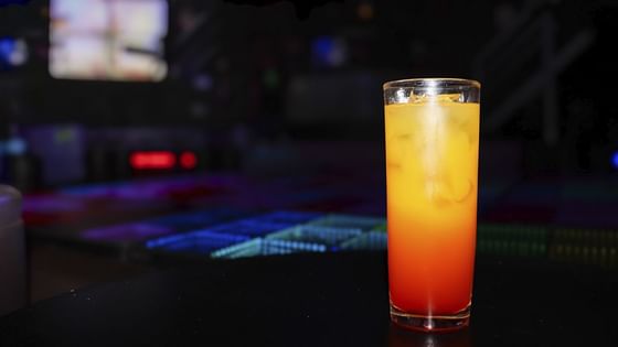 Vaso alto de cóctel de jugo de naranja y granadina en capas bajo luz tenue en El Rollo de Araiza Palmira