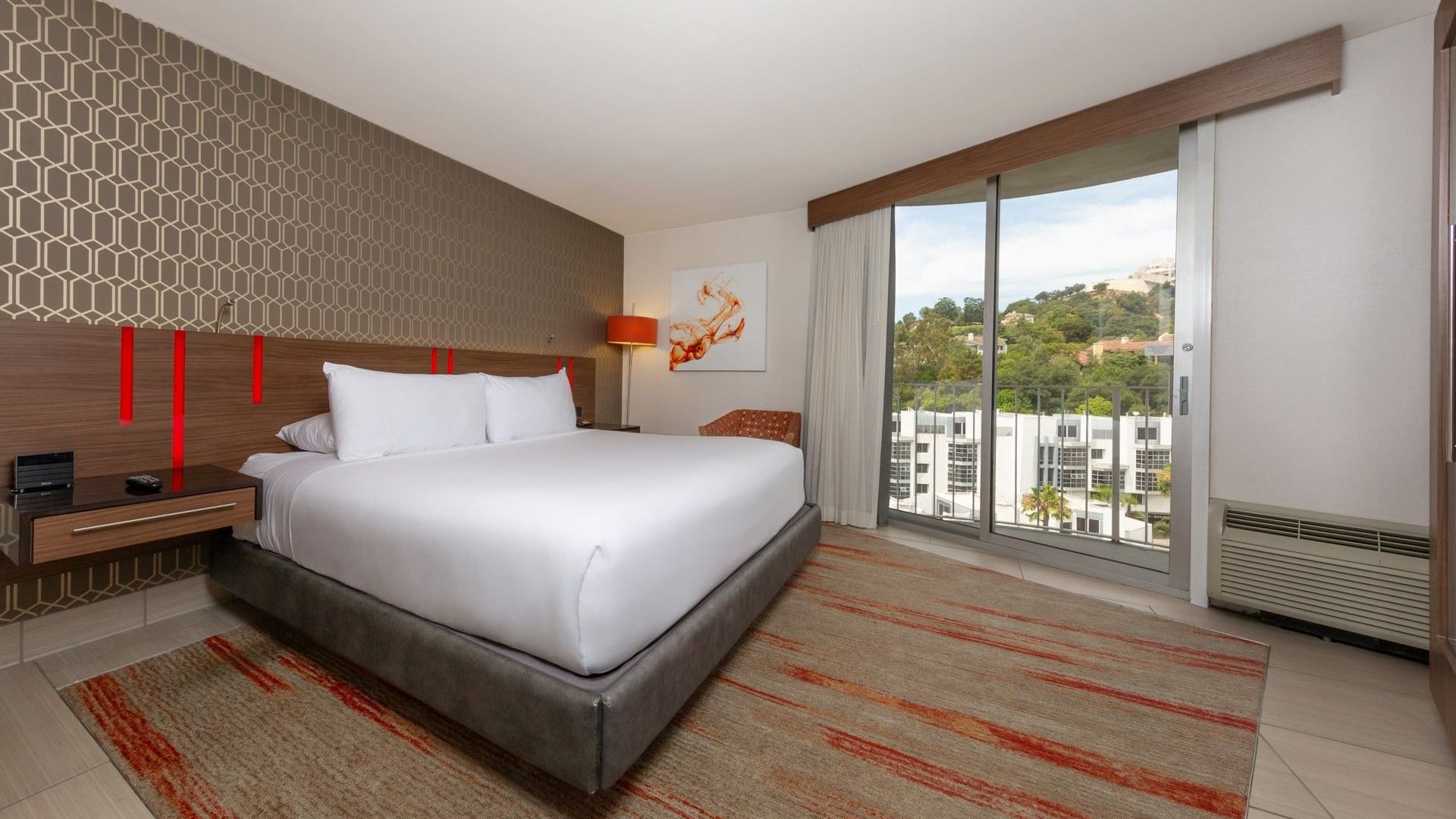 A hotel room with a large bed, a window with a view, and a rug