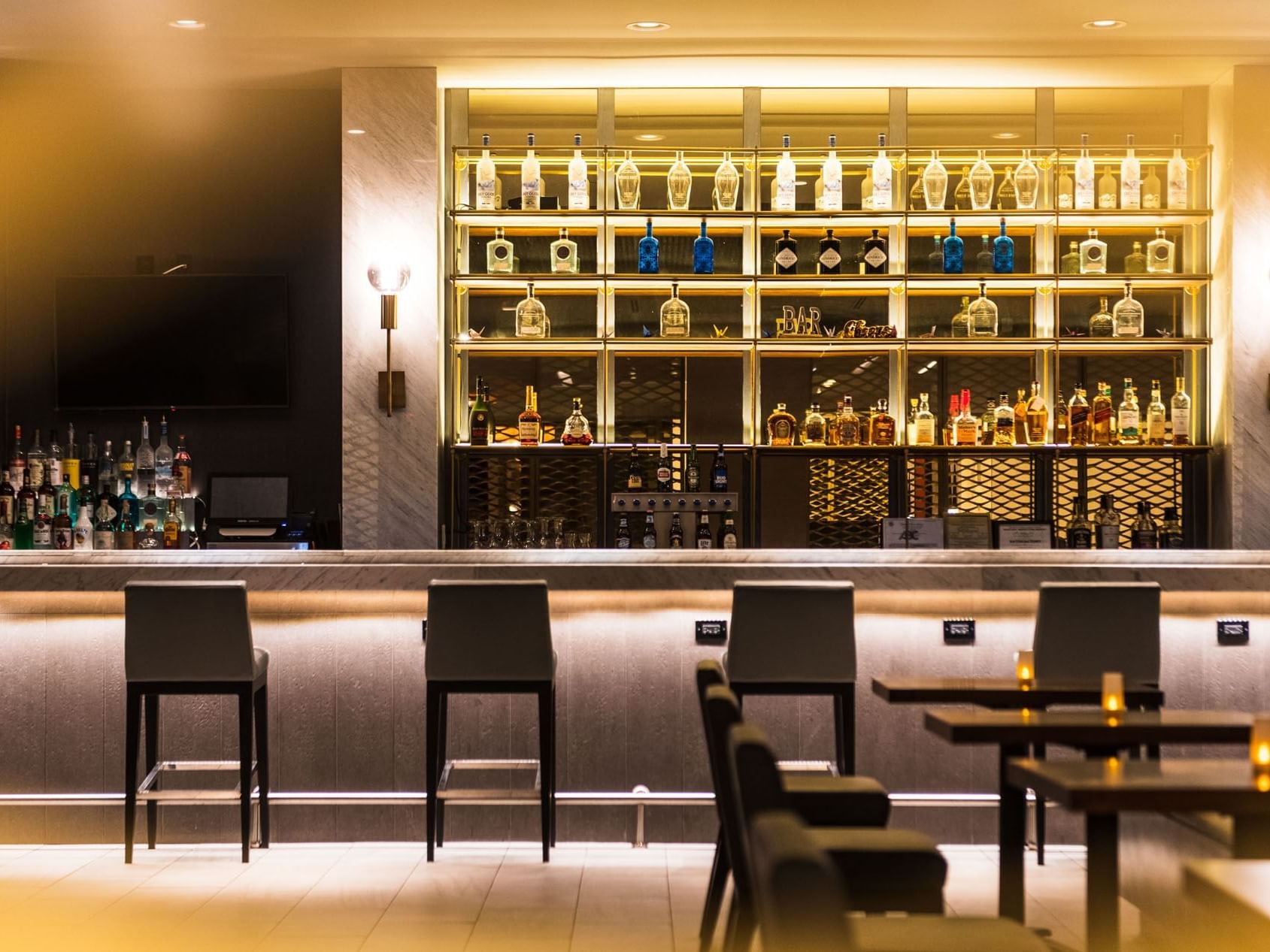 Well-lit shelves of liquor bottles and bar counter in Bogart's Lounge at APA Hotel Woodbridge