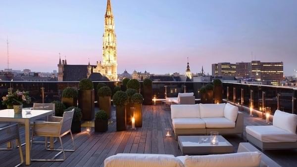 Outdoor terrace with modern white sofas placed by potted plants under a clear evening sky at Warwick Grand Place Brussels