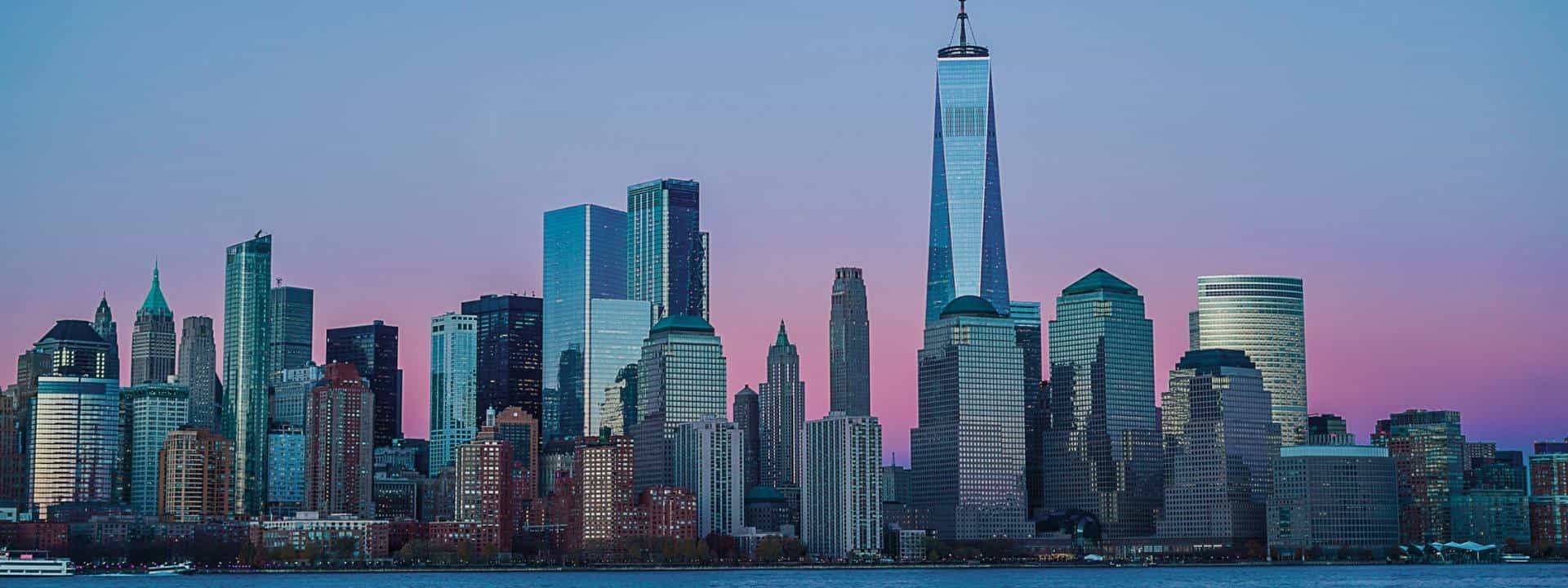 A city skyline with many skyscrapers and a body of water in front of it.