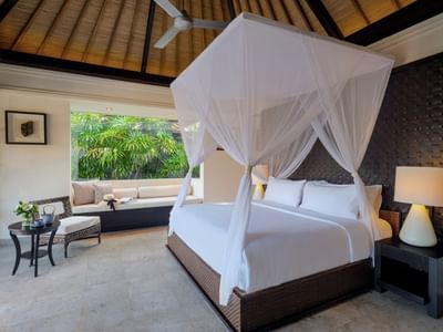 Elegant bedroom with canopy bed, couch, and tropical view at Peppers Seminyak