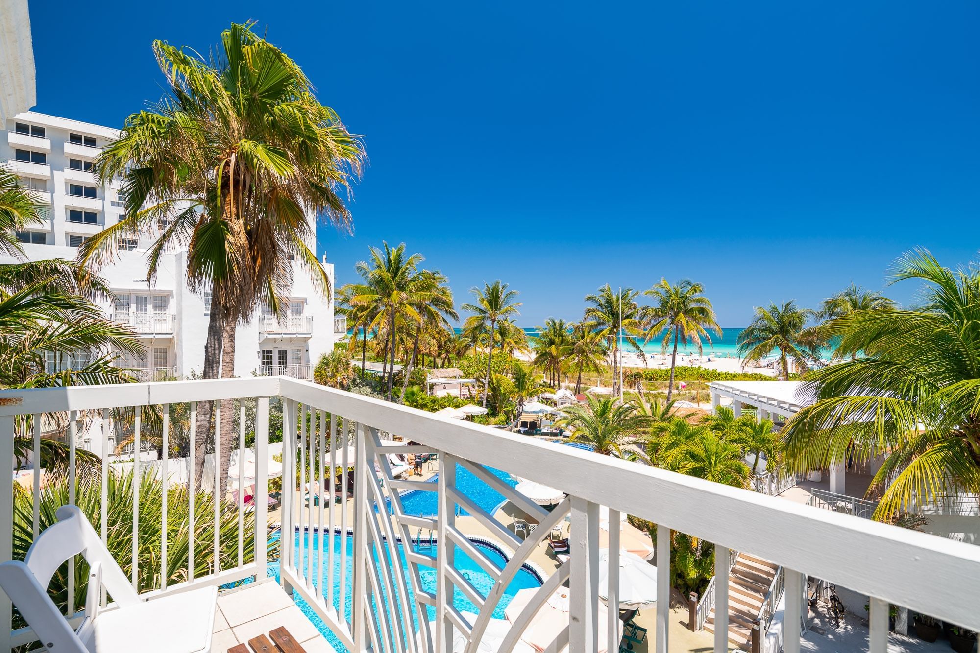 A balcony view of a hotel pool and beach with palm trees