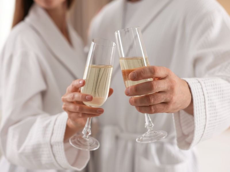 Couple in robes clinking sparkling wine glasses for a romantic getaway package.