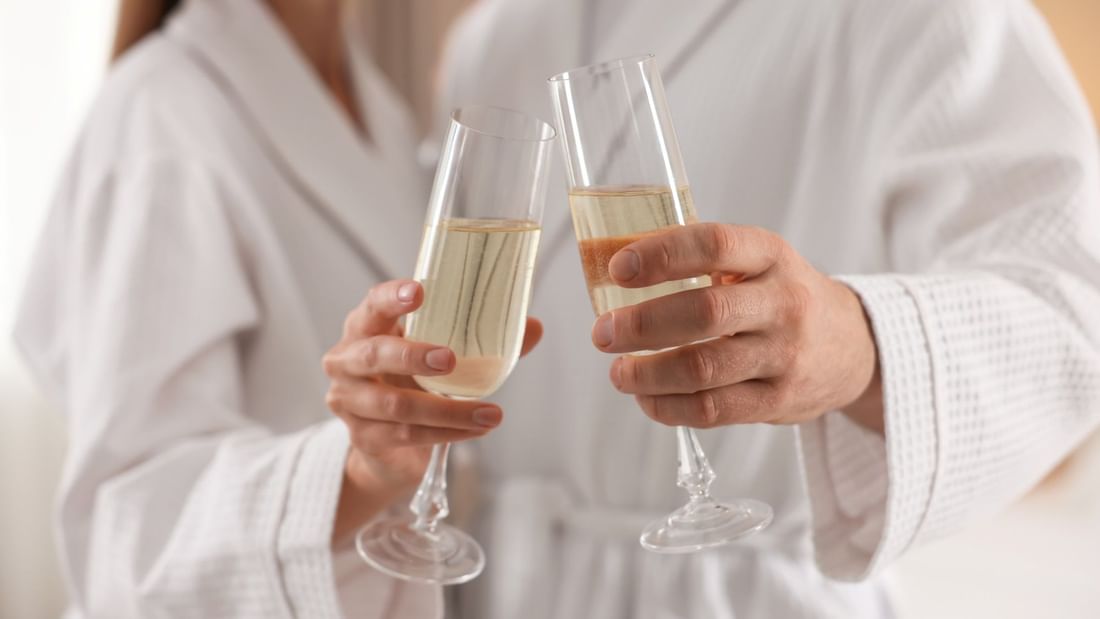 Couple in robes clinking sparkling wine glasses for a romantic getaway package.