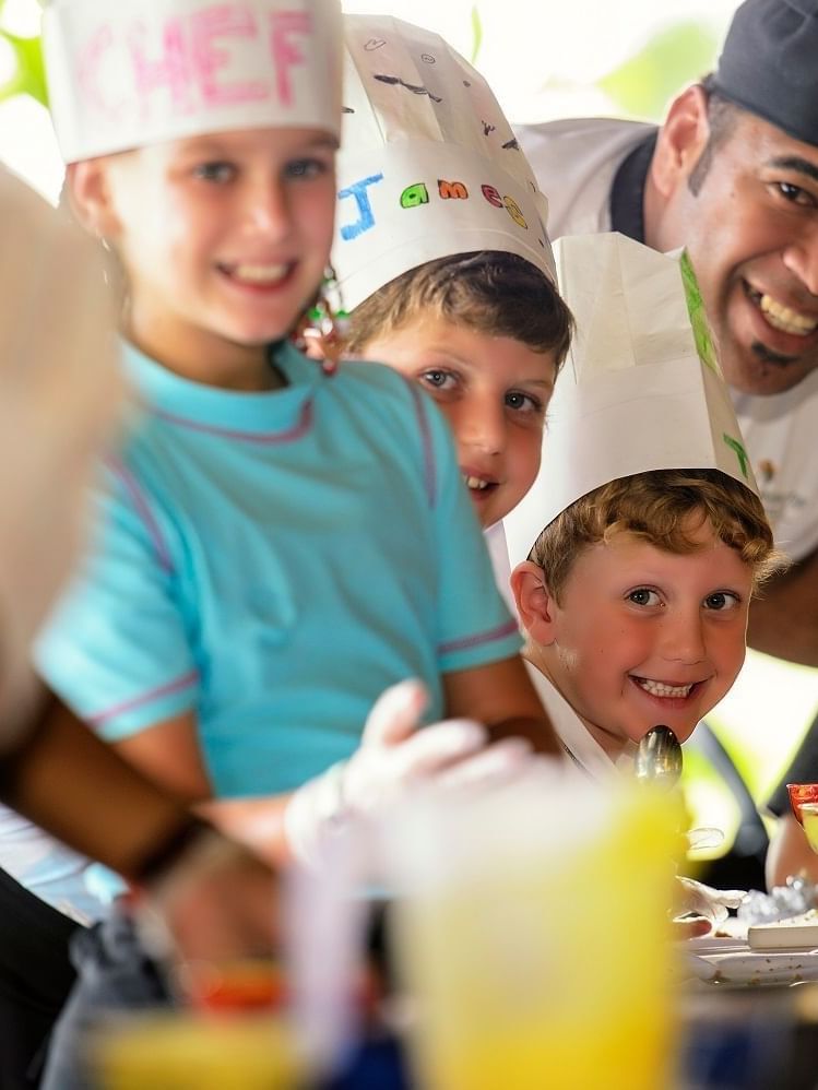 Smiling children in chef hats by a smiling instructor under a bright patio at The Naviti Resort - Fiji