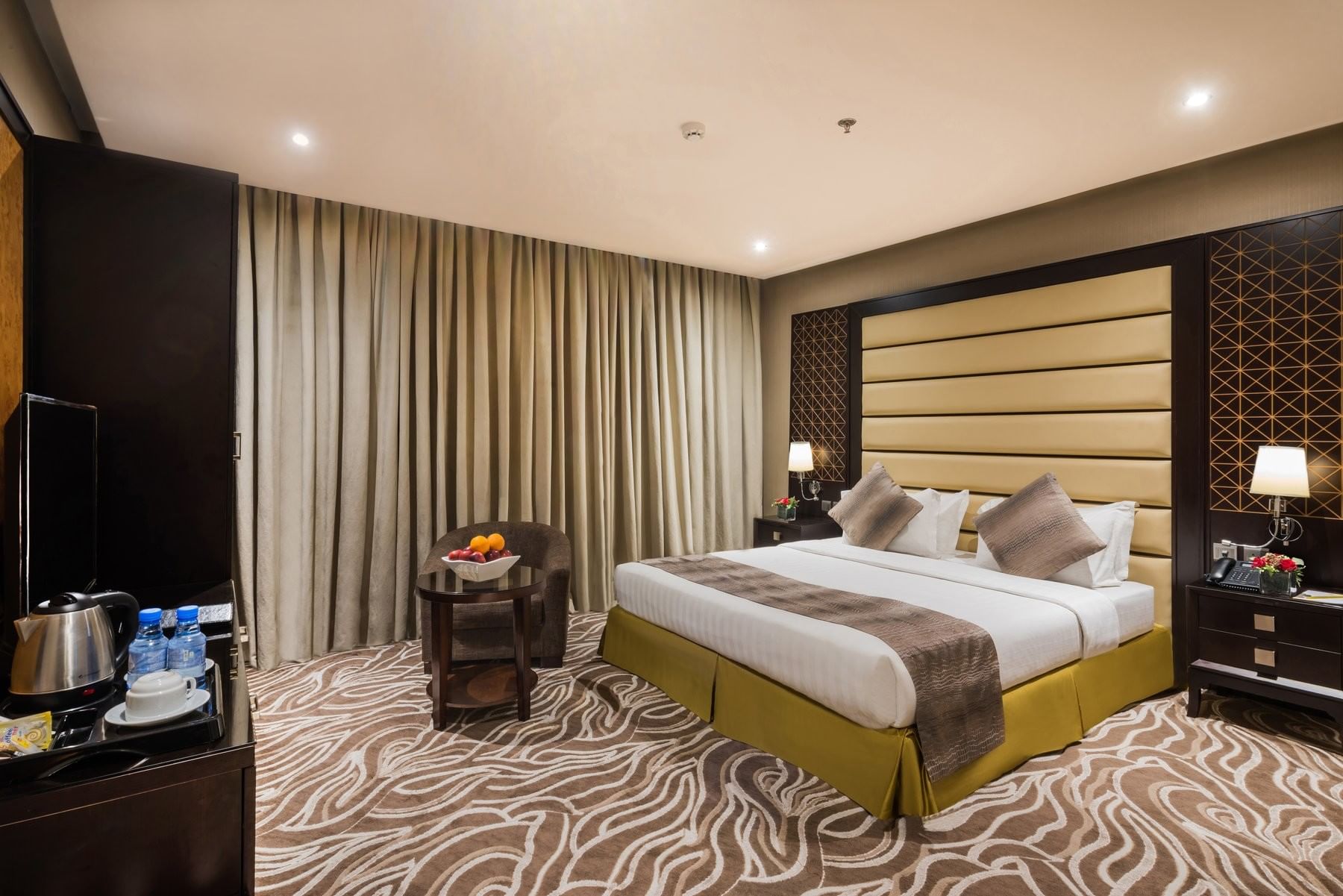 Fruit bowl on a table by an chair under heavy drapes near the bed in Deluxe King / Twin Room at Naviti by Warwick Al Khobar