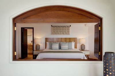 Wooden archway frames view of a bedroom with bed, nightstands, and decorative wall hanging.