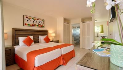 Twin beds with vibrant orange runners and colorful wall art in the Superior Room at Worthing Court Apartment