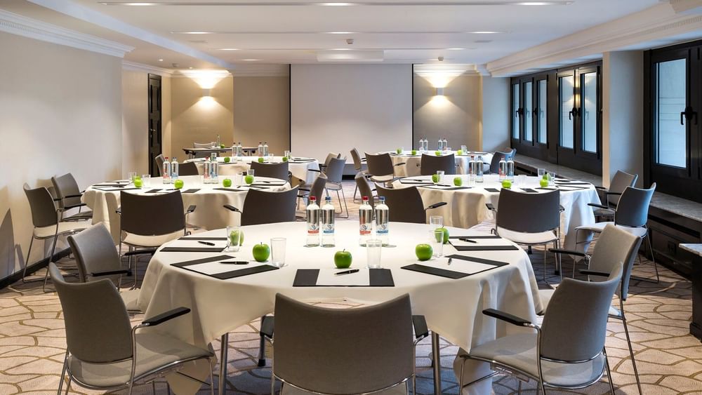 Des tables rondes et des chaises disposées avec élégance dans la salle de réception Barsey III de l'hôtel Barsey by Warwick à Bruxelles.