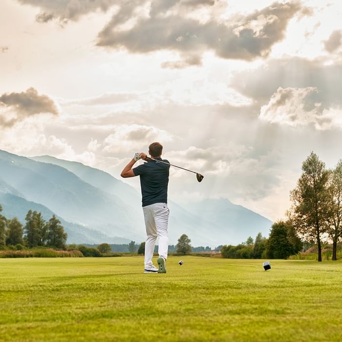 Golfspieler schwingt Golfschläger auf grünem Golfplatz mit Bergen im Hintergrund bei Falkensteiner Hotel & Spa Carinzia