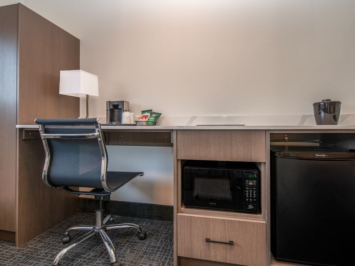 A hotel room with chair, work desk, microwave, mini-fridge, and a coffee maker.