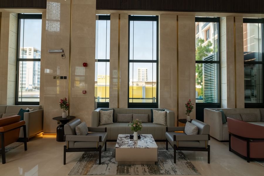 Grey sofas around a marble coffee table across tall windows in the lobby lounge area at Naviti by Warwick Jeddah