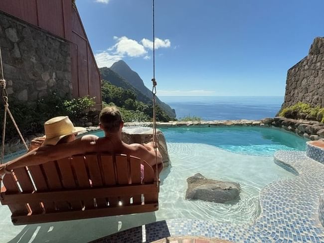 Couple relaxing on a wooden swing overlooking a private pool with pitons view in Ladera