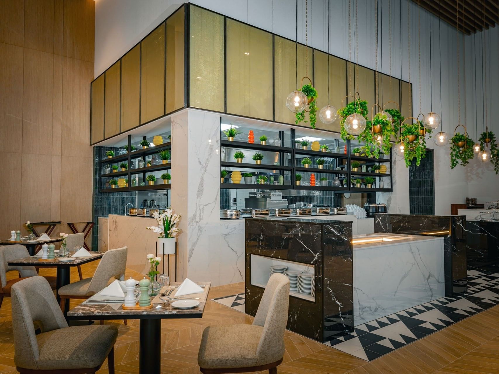 A modern restaurant with tables, chairs, a marble counter, hanging plants, and a kitchen in the background.