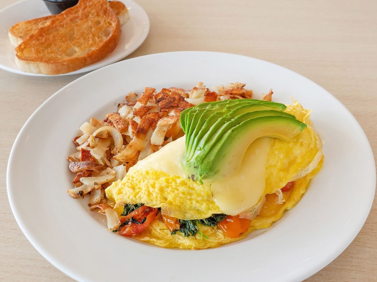 Plate with omelet, avocado, and hash browns next to plate with toast.