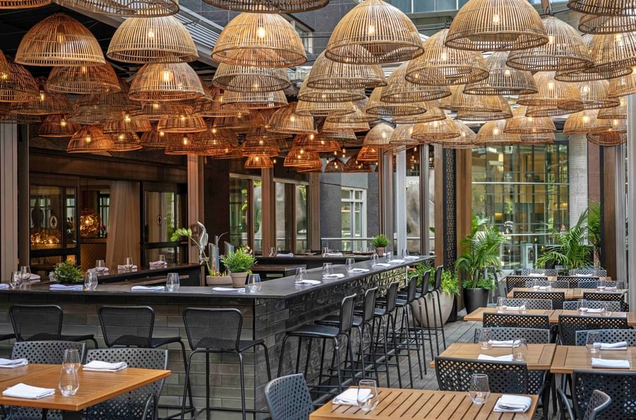 Outdoor bar area with bamboo lamps hanging over dark stone counters and tables at Warwick Le Crystal Montreal