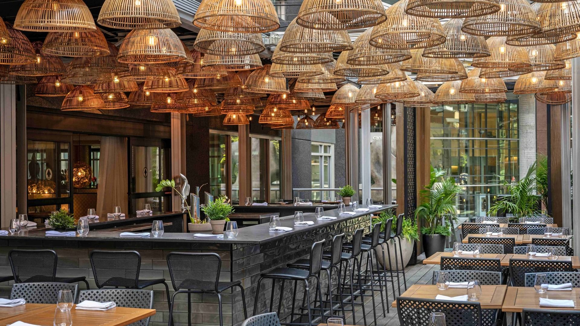 Outdoor bar area with bamboo lamps hanging over dark stone counters and tables at Warwick Le Crystal Montreal