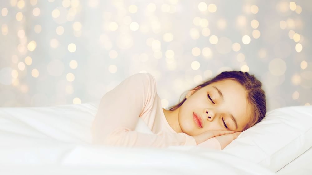 young girl sleeping peacefully in a white bed under glowing bokeh lights at Warwick Hotels and Resorts
