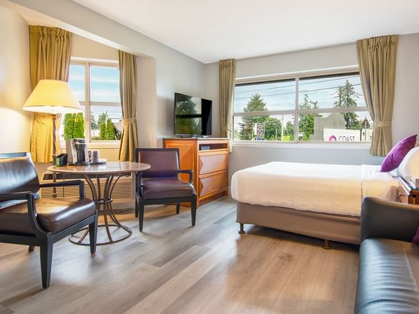 A hotel studio suite with queen bed, couch, TV, table and chairs