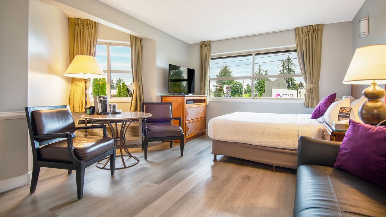 A hotel studio suite with queen bed, couch, TV, table and chairs
