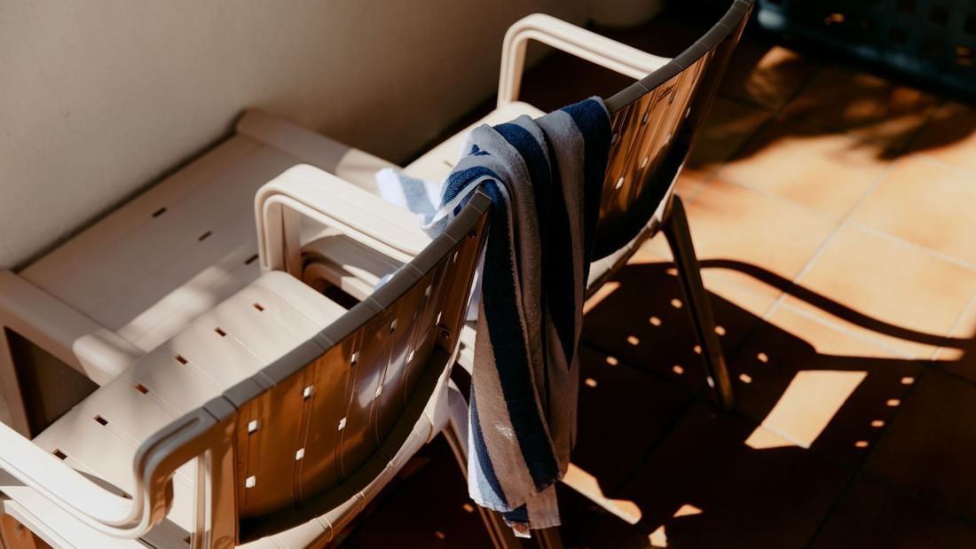 Two chairs with a blue and white striped towel draped over one, on a tiled patio.