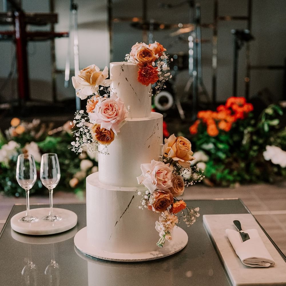 Close-up of three-tiered wedding cake with floral decorations, champagne glasses and cutlery on table at Crown Towers Sydney